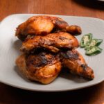 Spicy grilled chicken drumsticks on a plate with jalapeno slices.
